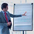 businessman-leading-meeting-at-flip-chart-in-conference-room-G1TCD3